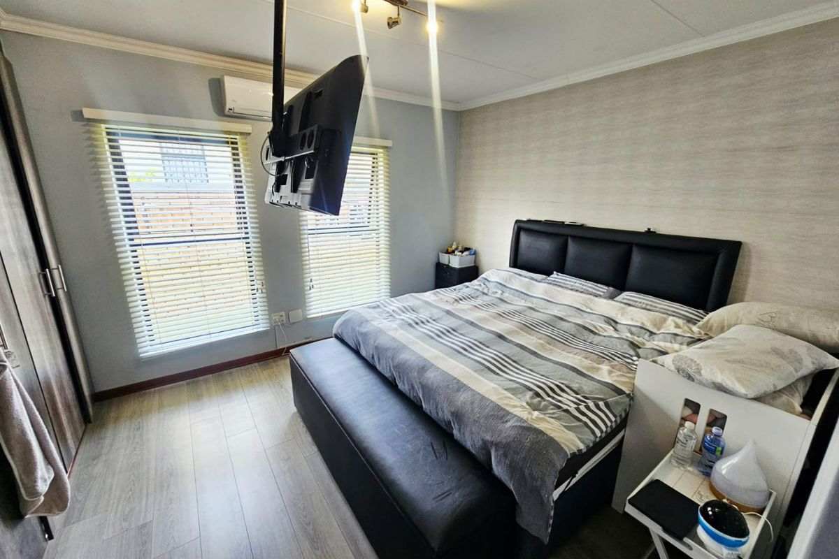 A well-maintained bedroom featuring laminate flooring, dual windows with venetian blinds, a built-in wardrobe, and a wall-mounted air conditioning unit.