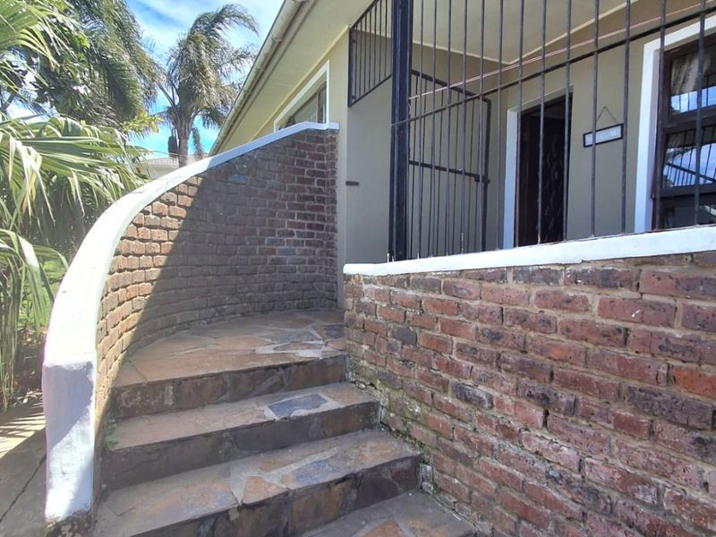 Exterior view of the front entrance featuring a curved brick staircase with stone paving and a secure metal gate.