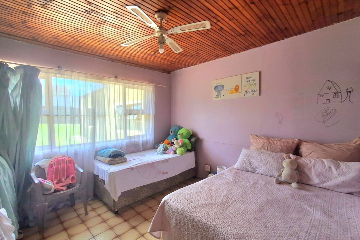 A bedroom featuring a timber slat ceiling, ceiling fan, and tiled flooring, currently showing signs of wear on the walls.