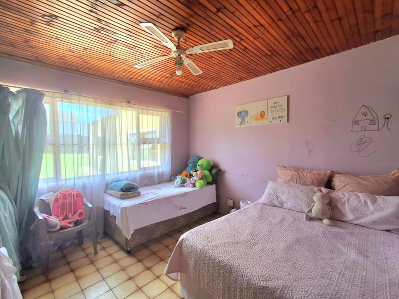 A bedroom featuring a timber slat ceiling, ceiling fan, and tiled flooring, currently showing signs of wear on the walls.