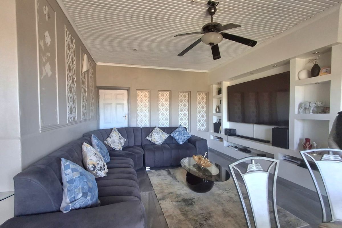 Living room featuring built-in shelving, decorative wall paneling, tiled flooring, and a ceiling fan.