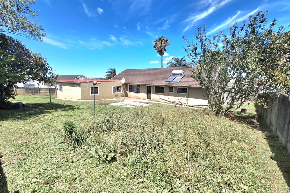 Rear view of the house featuring a tiled roof with solar water heating, a paved patio area, and a large, overgrown garden space.