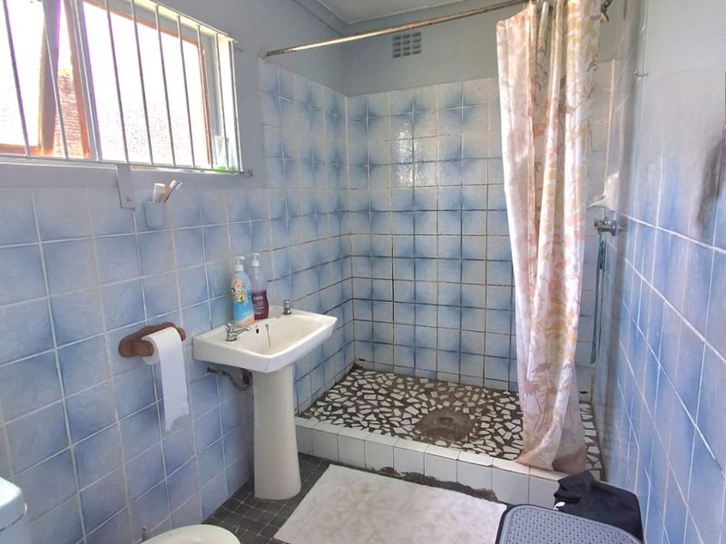 A functional bathroom featuring a pedestal basin, toilet, and a shower cubicle with tiled walls and flooring, requiring cosmetic updates.