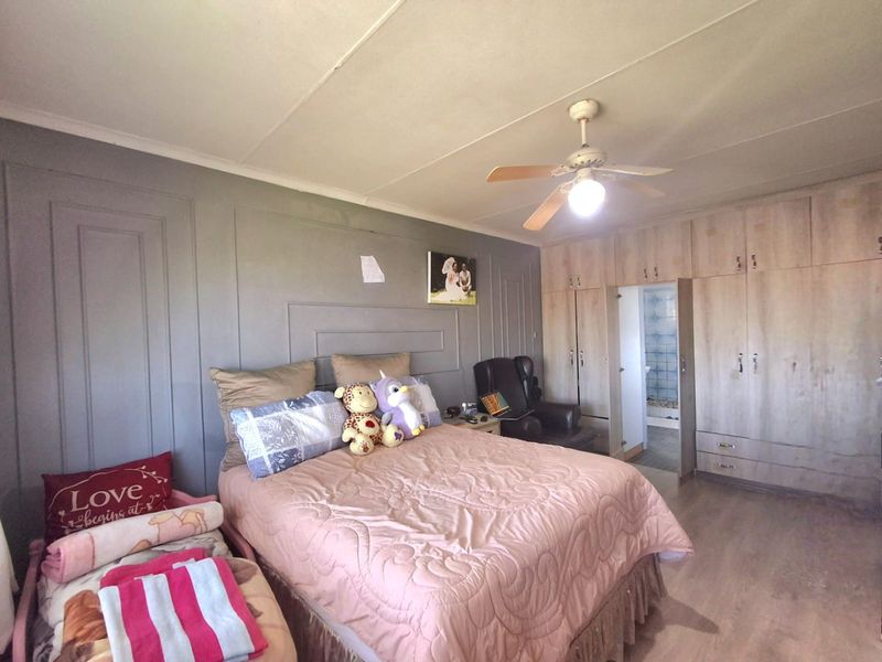 A bedroom featuring built-in cupboards, a ceiling fan, and laminate flooring, with a panelled feature wall and an adjoining en-suite bathroom.
