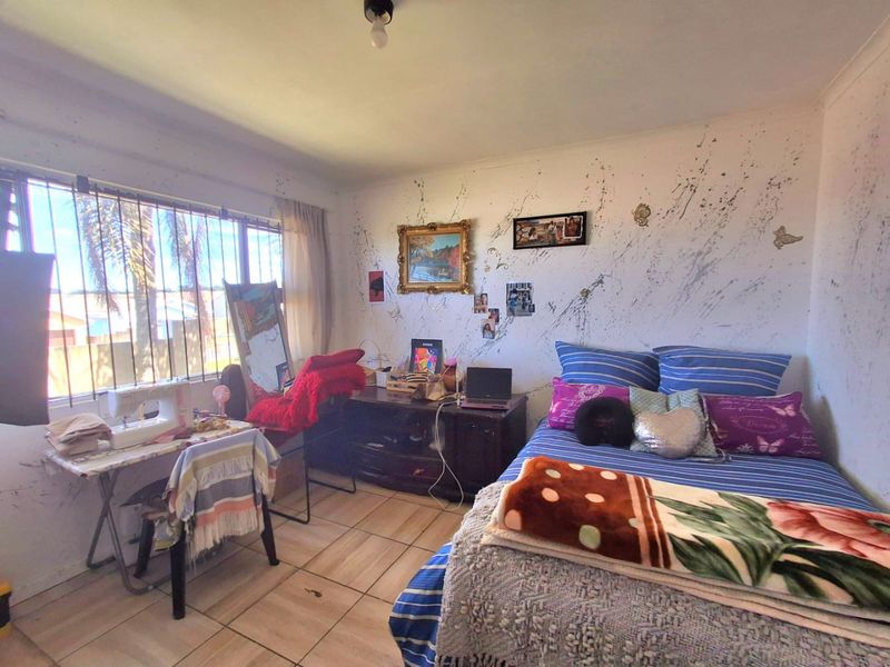 A bedroom featuring tiled flooring and security bars on the window, currently requiring cosmetic attention to the wall finishes.