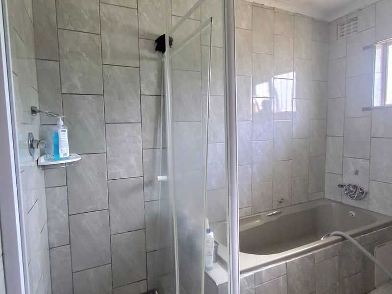 A functional bathroom featuring a separate shower enclosure with a pebble floor, a built-in bathtub, and neutral wall tiling throughout.
