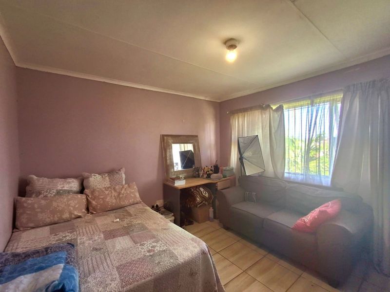 A bedroom featuring tiled flooring and a window with security bars, requiring cosmetic updates to the walls and ceiling.