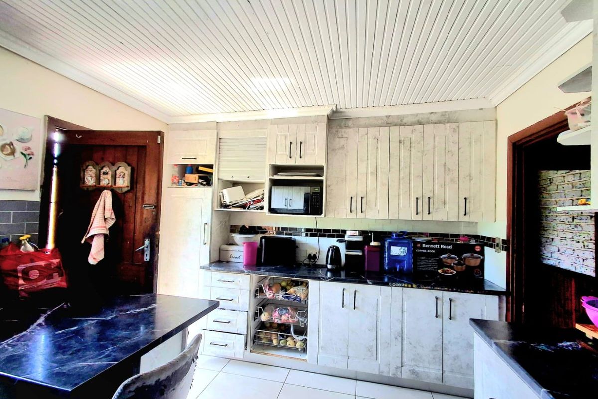 A functional kitchen featuring built-in cabinetry, dark laminate countertops, tiled backsplash, and tiled flooring with a distinctive tongue and groove ceiling finish.