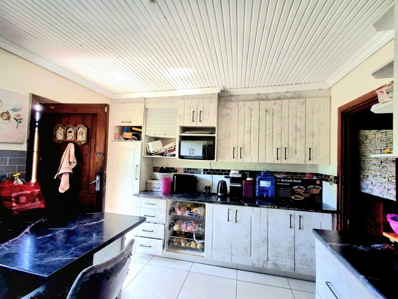A functional kitchen featuring built-in cabinetry, dark laminate countertops, tiled backsplash, and tiled flooring with a distinctive tongue and groove ceiling finish.