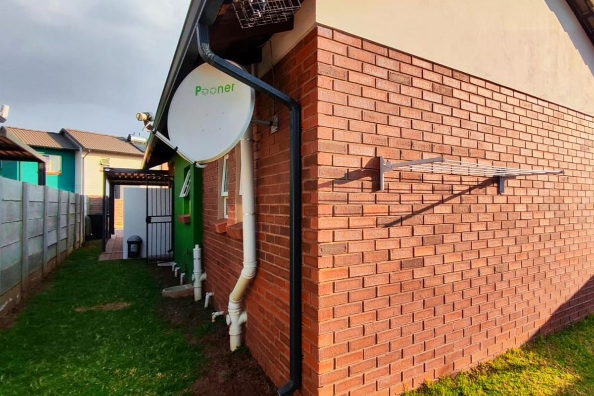 A view of the rear exterior of the house featuring face brick walls, a satellite dish, and a wall-mounted drying rack.