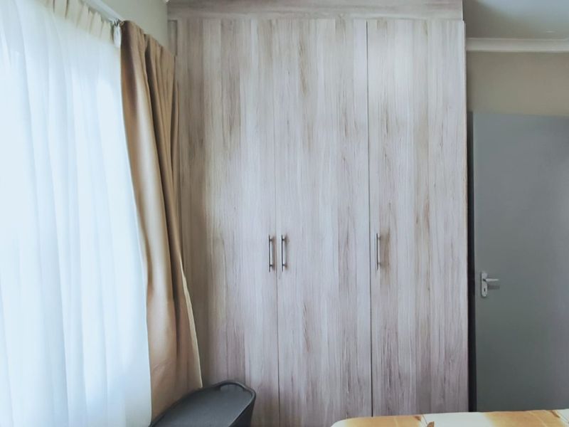 A bedroom featuring a large, light wood-grain built-in wardrobe and a window with curtains.