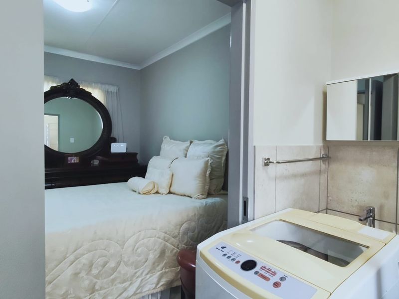 A functional laundry area featuring a wall-mounted cabinet and tiled splashback, with a direct view into the adjacent bedroom.