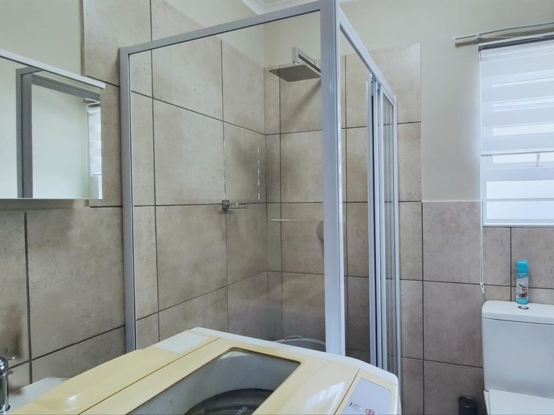 A functional bathroom featuring a glass-enclosed shower with a rain shower head, tiled walls, a wall-mounted mirror cabinet, and a standard toilet.