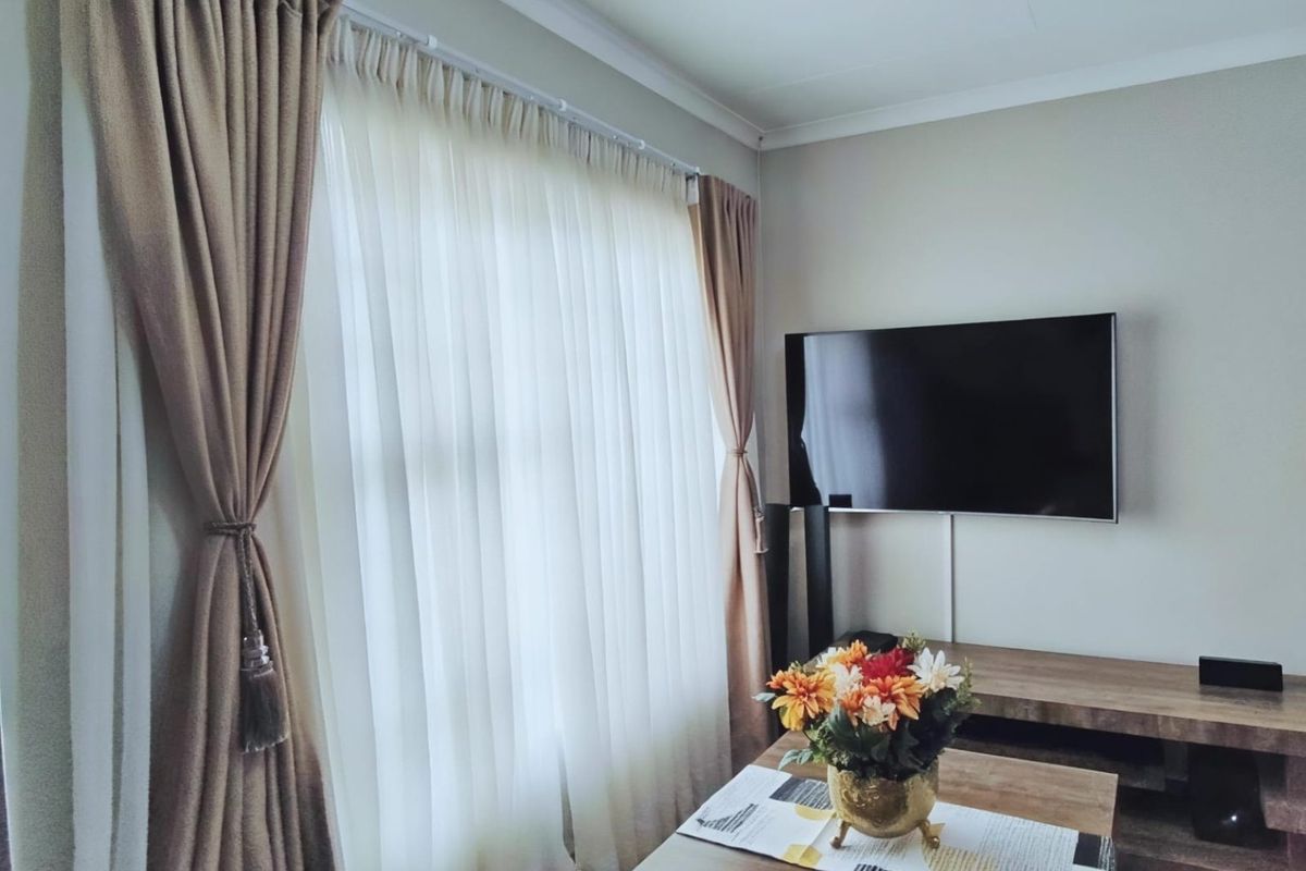 A well-maintained living room featuring a wall-mounted television and floor-to-ceiling window treatments.