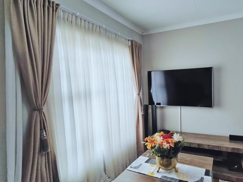 A well-maintained living room featuring a wall-mounted television and floor-to-ceiling window treatments.