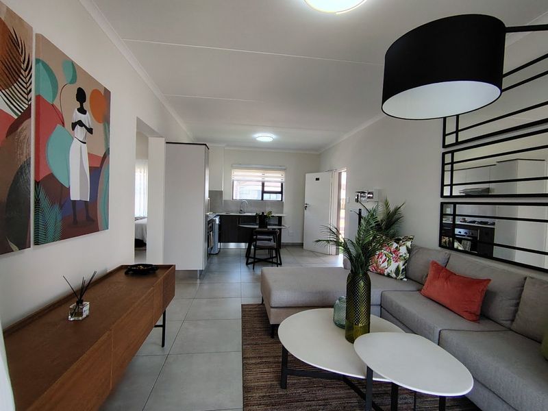 A well-maintained open-plan living and kitchen area featuring neutral tiled flooring, modern cabinetry, and a functional layout suitable for contemporary apartment living.