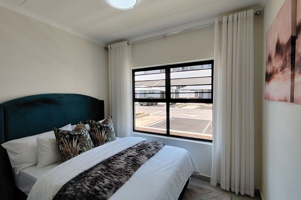 A well-maintained bedroom featuring tiled flooring, a large window with security bars, and neutral wall finishes.