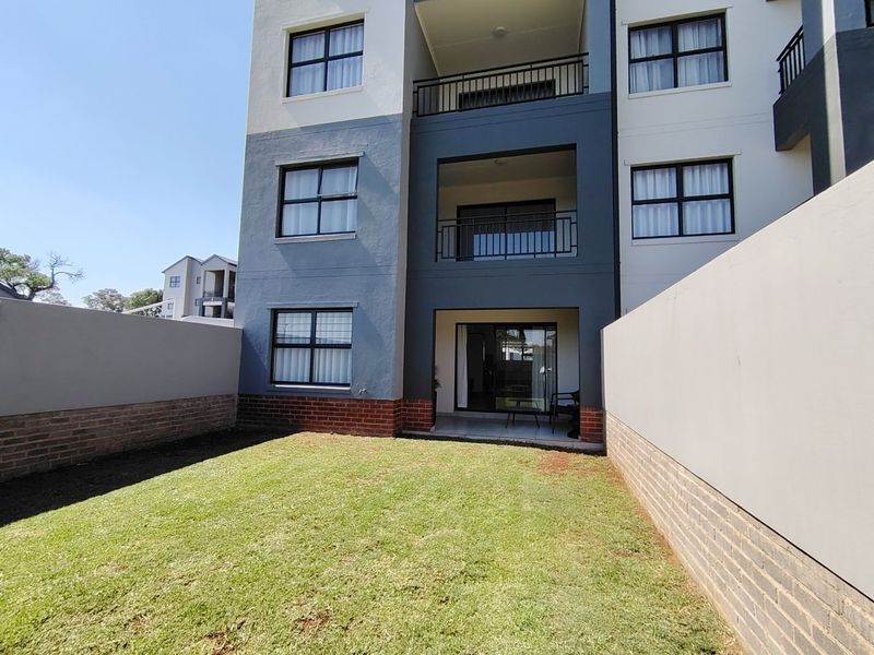 Rear view of a modern apartment building featuring a private ground-floor garden, brick boundary walls, and upper-level balconies with metal railings.