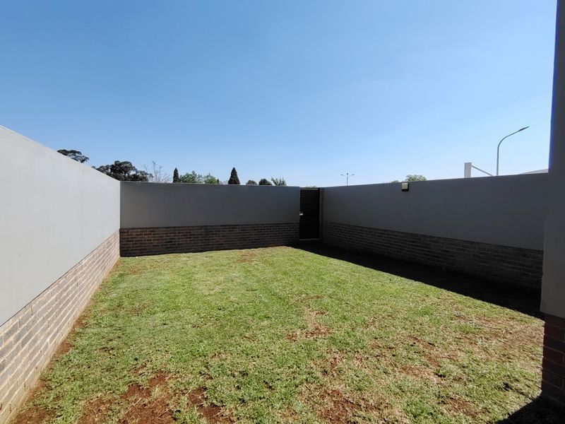A private, enclosed garden area featuring a well-maintained lawn, brick-based boundary walls, and a secure pedestrian gate.