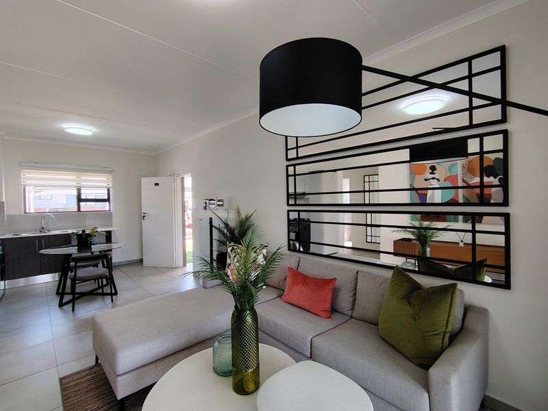 An open-plan living and kitchen area featuring tiled floors, modern cabinetry, and a decorative wall mirror, creating a bright and functional living space.