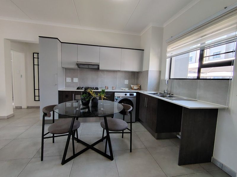 Modern kitchen featuring dark wood and light grey cabinetry, stone countertops, gas hob, extractor fan, and integrated washing machine with tiled flooring.