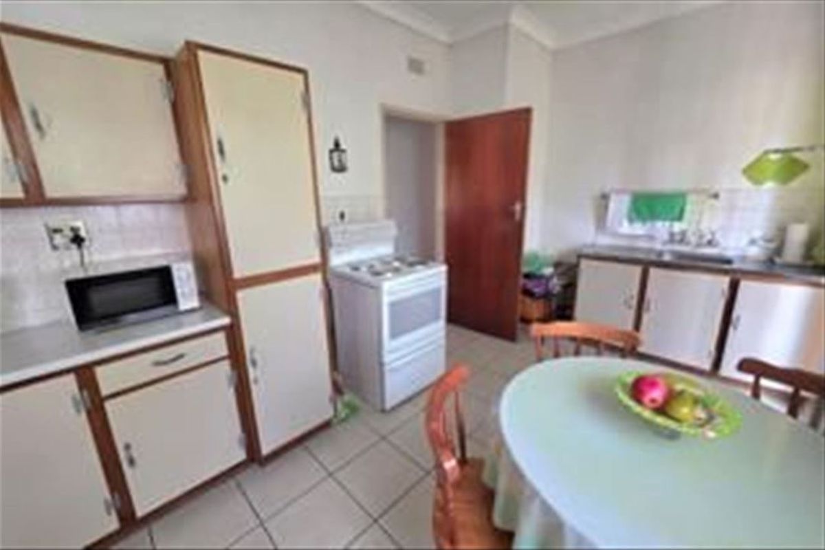 A dated kitchen featuring original cabinetry, tiled flooring, a freestanding stove, and a functional sink area, offering potential for modern renovation.
