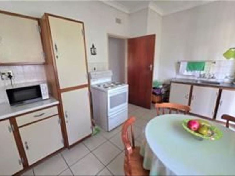 A dated kitchen featuring original cabinetry, tiled flooring, a freestanding stove, and a functional sink area, offering potential for modern renovation.