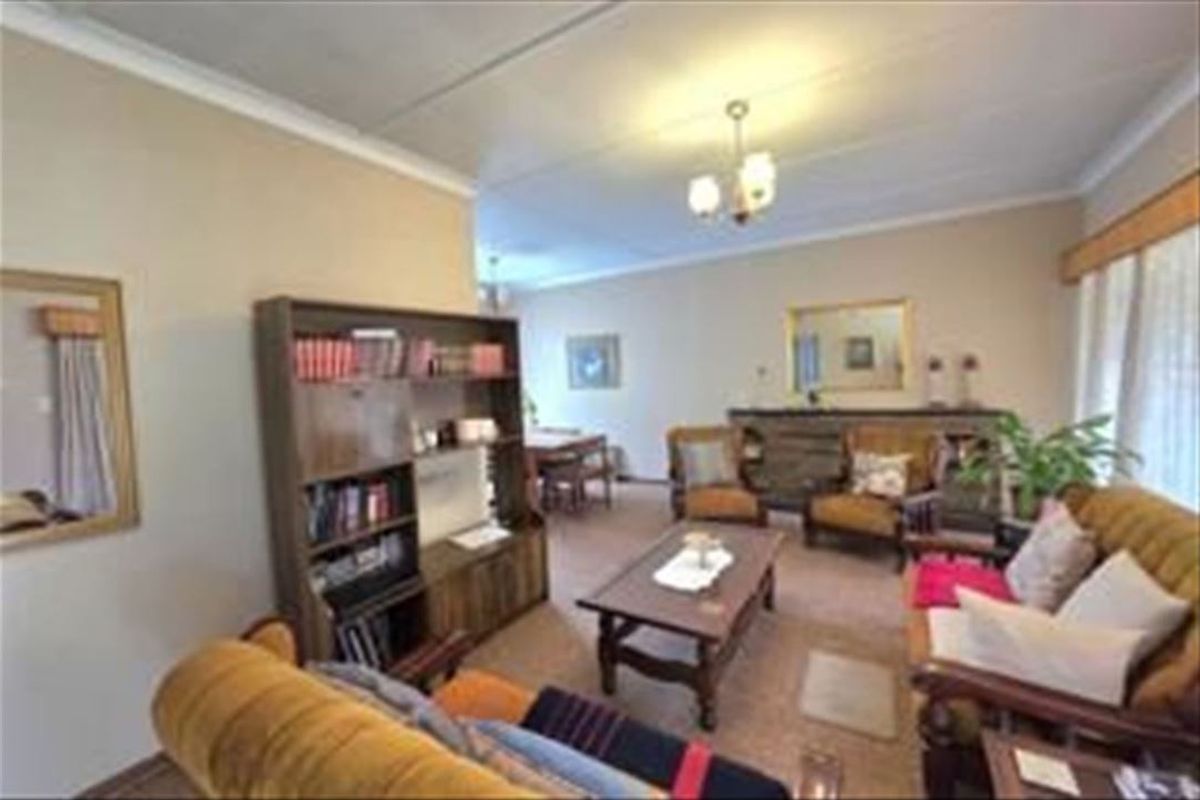 A spacious living room area featuring neutral wall tones, ceiling cornicing, and a central light fixture, offering a comfortable and functional living space.