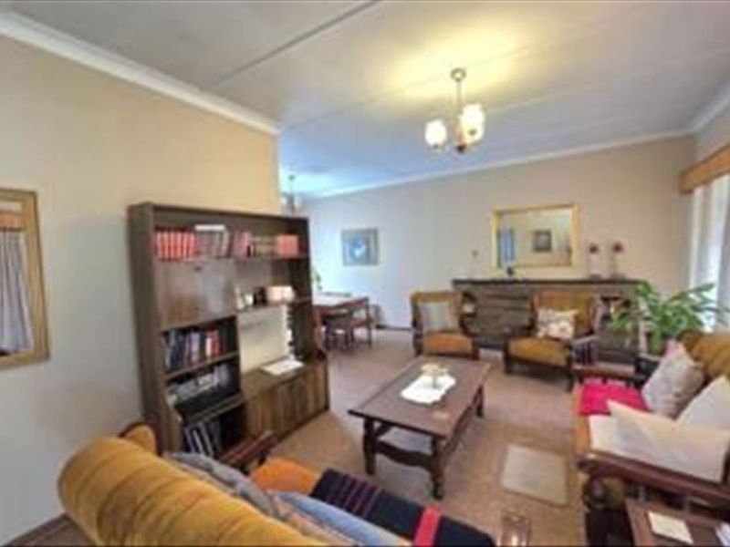 A spacious living room area featuring neutral wall tones, ceiling cornicing, and a central light fixture, offering a comfortable and functional living space.