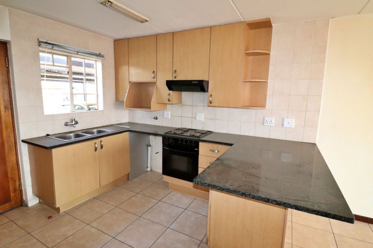 A functional kitchen featuring light wood cabinetry, dark granite countertops, a built-in oven with hob, and a double basin sink with tiled splashbacks.