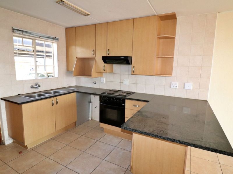 A functional kitchen featuring light wood cabinetry, dark granite countertops, a built-in oven with hob, and a double basin sink with tiled splashbacks.
