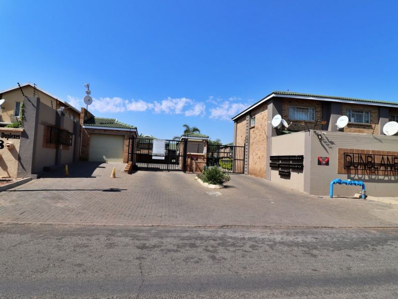 Front entrance view of Dunblane complex featuring paved driveway, secure gated access, and brick facade apartment buildings.
