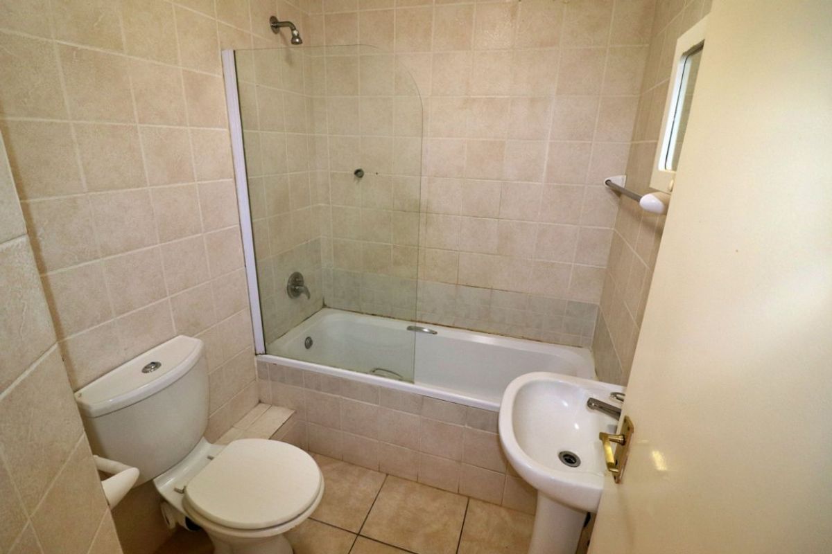 A compact bathroom featuring a bathtub with a glass shower screen, pedestal basin, and toilet, finished with neutral wall and floor tiling.