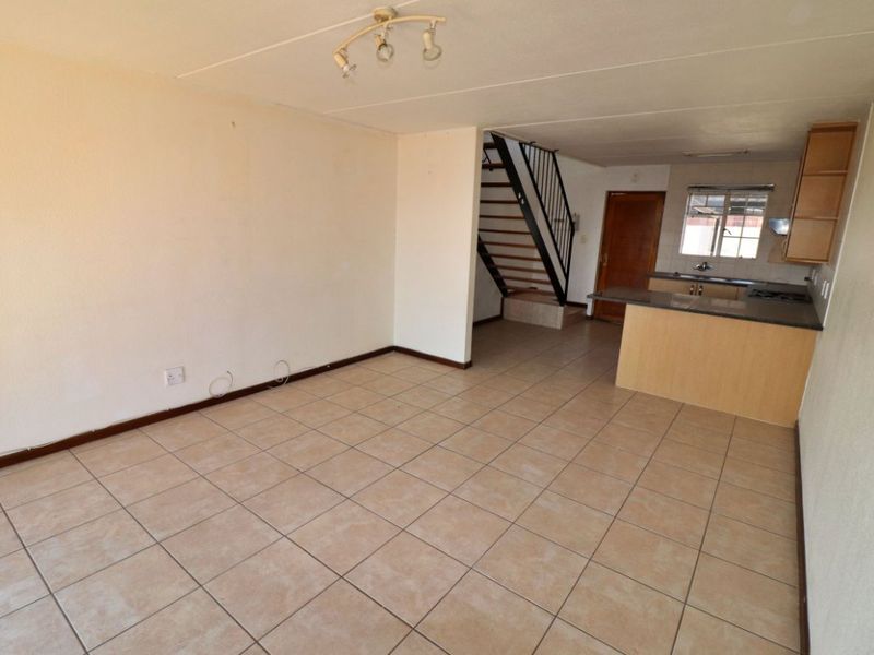 Open-plan living area featuring tiled flooring, a staircase, and an adjoining kitchen with built-in cabinetry and a breakfast counter.