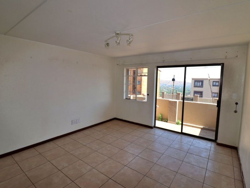 An empty living room featuring tiled flooring, a ceiling-mounted light fixture, and sliding glass doors leading to a balcony with exterior views.