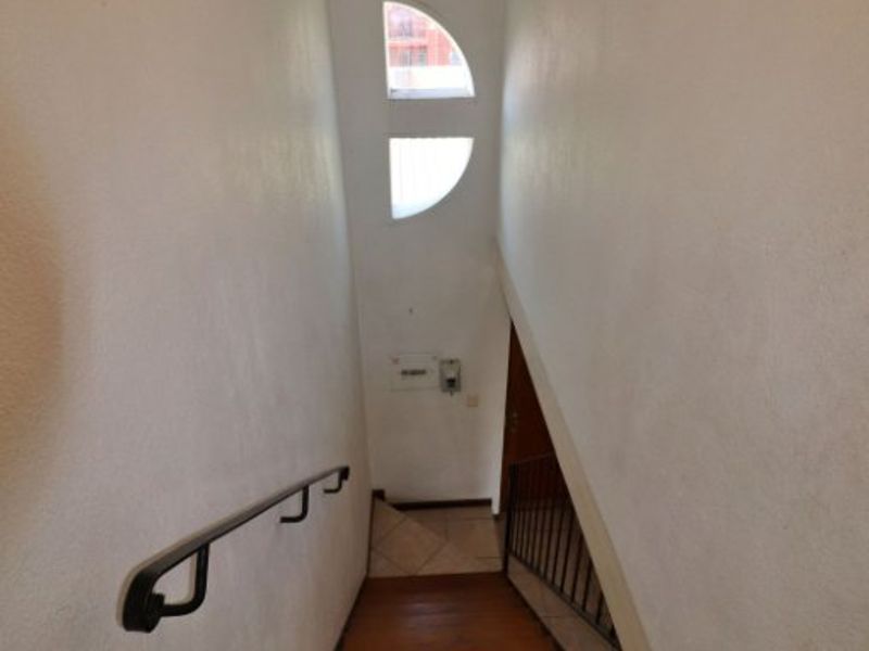 A staircase featuring wooden treads, a metal handrail, and a unique semi-circular window providing natural light to the hallway area.