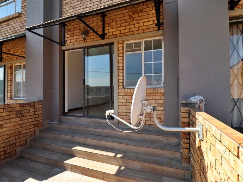 A private balcony area featuring tiled flooring, brick facade, sliding glass door access, and a mounted satellite dish.