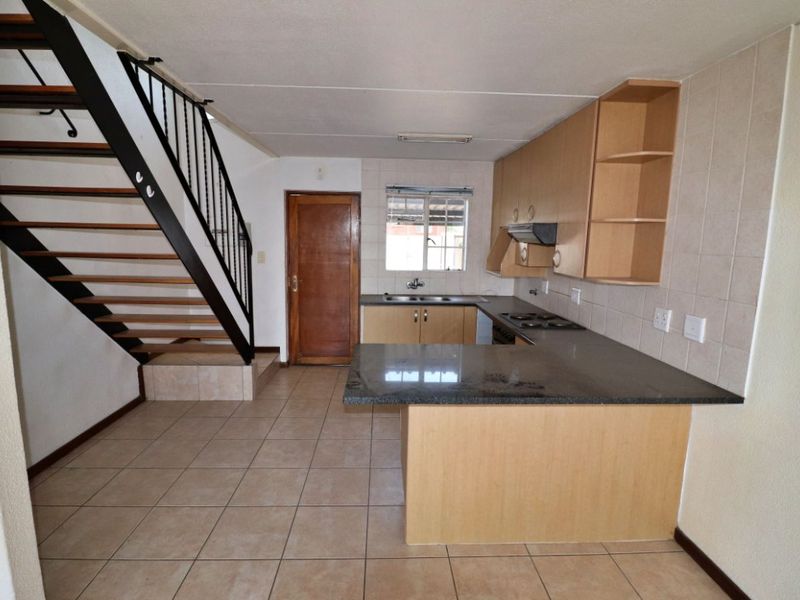 Open-plan kitchen featuring granite countertops, built-in cabinetry, and an integrated hob, adjacent to an internal staircase with metal railings.