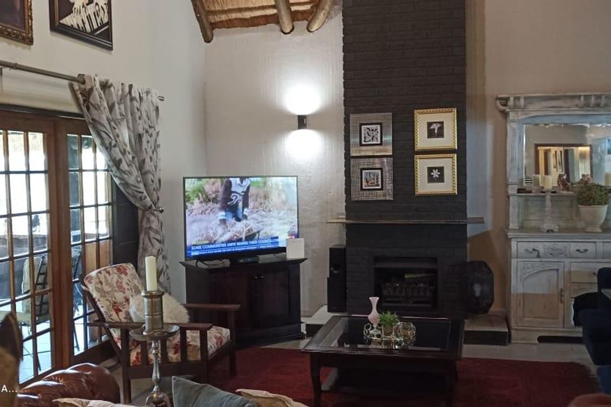 Spacious living room featuring a high vaulted ceiling with exposed timber beams, a prominent dark brick fireplace, and large glass sliding doors to the patio.