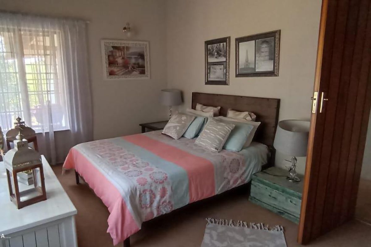 A comfortable bedroom featuring a large window with natural light, neutral wall finishes, and a wooden door leading to an adjacent space.