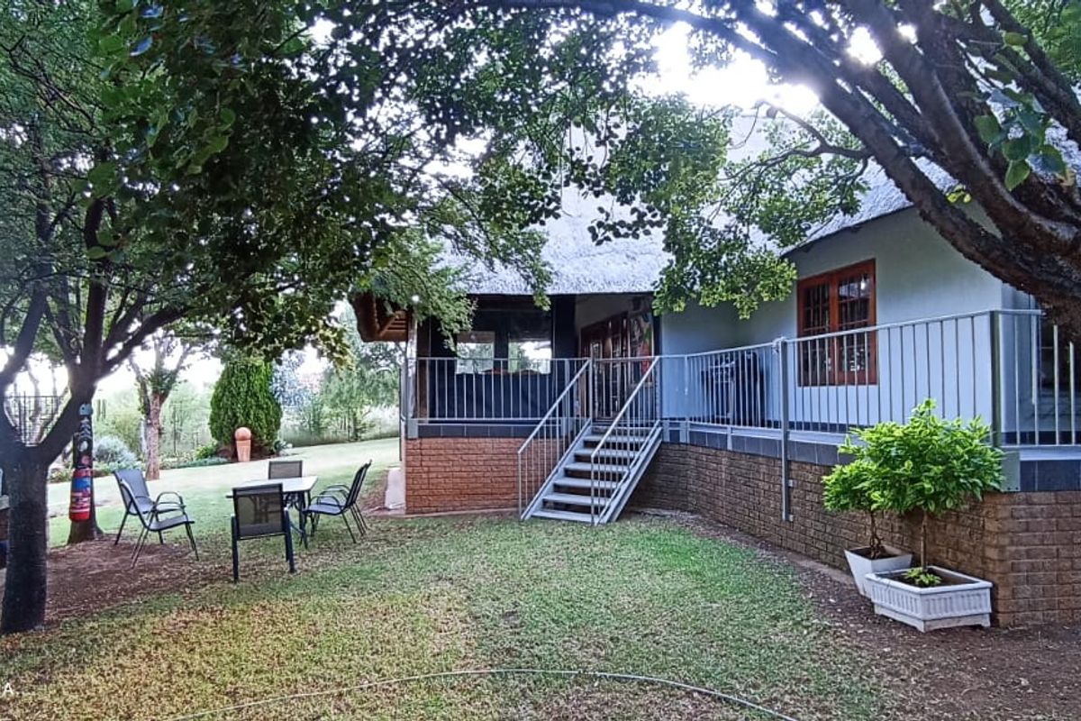 A rear view of the house featuring a thatched roof, brick base, metal staircase, and a paved outdoor area with a built-in brick braai.