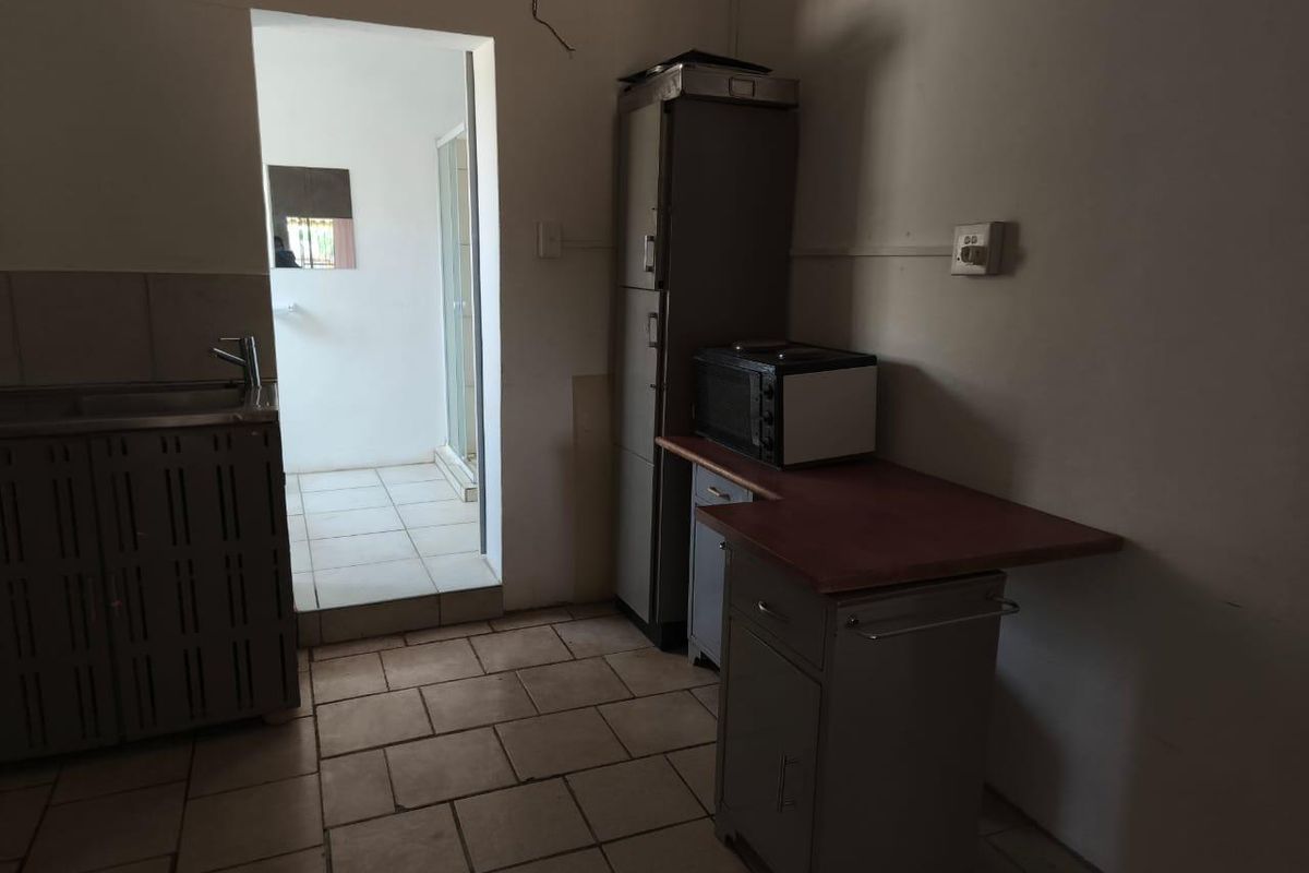 A functional kitchen area featuring tiled flooring, built-in cabinetry, and a stainless steel sink, with an adjacent doorway leading to a bathroom area.