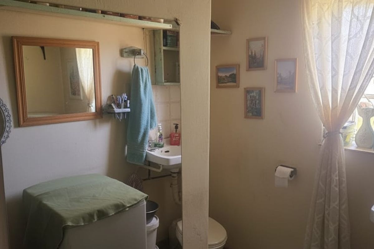 A functional bathroom featuring a wall-mounted basin and toilet, with tiled flooring and natural light from a window.