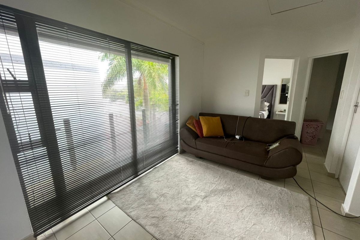 A living room featuring large sliding glass doors with fitted blinds, tiled flooring, and access to an adjacent bedroom.