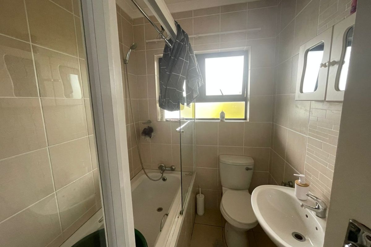 A functional bathroom featuring a bathtub with shower attachment, pedestal basin, and toilet, finished with neutral wall and floor tiling.