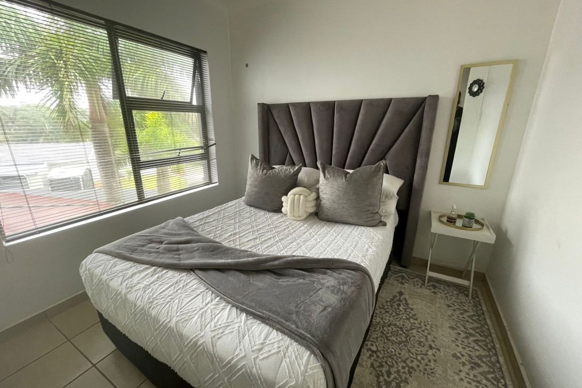 A well-lit bedroom featuring tiled flooring, a large window with fitted blinds, and neutral wall finishes.