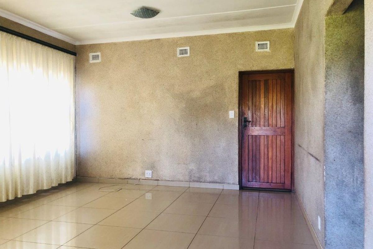 An empty living room featuring tiled flooring, a solid timber door, and textured wall finishes, offering a blank canvas for renovation.