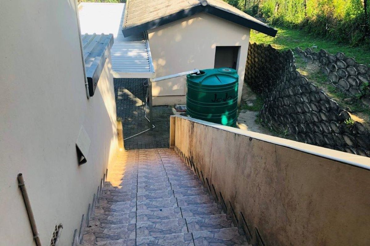 Exterior view showing a tiled staircase leading down to a rear yard area featuring a water storage tank and paved pathway.