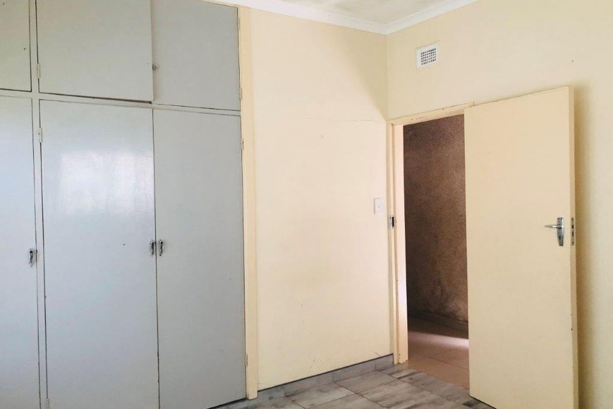 A bedroom featuring built-in cupboards, tiled flooring, and a doorway leading to an adjacent space, requiring cosmetic updates to modernize the interior finishes.
