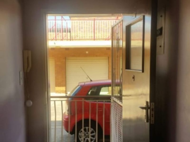 An apartment entrance area featuring a security gate and intercom system, providing direct access to the exterior parking area.